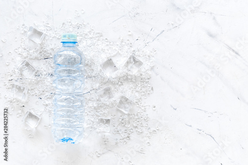 Pile of ice cubes and bottle on marble bar desk background top view copyspace