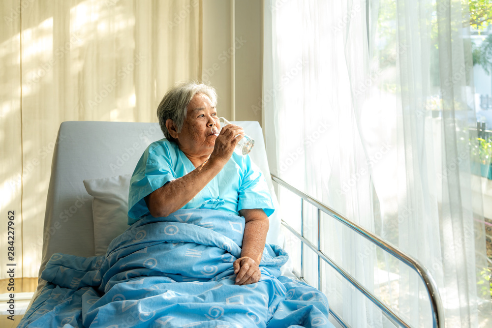 slap af Rå Transformer Asian elderly woman sitting and holding glass of water in bed at hospital.  Stock-foto | Adobe Stock