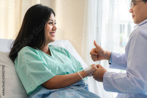 Hand of man doctor reassuring his female patient with thump up in bed at hospital. Medical ethics and trust concept..