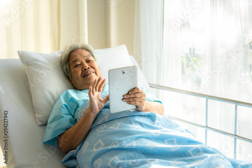 Asian senior using a digital touch screen tablet  she is connecting online and social networking while she illness in hospital.