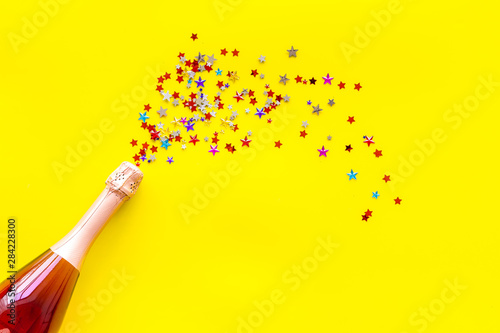 Champagne bottle with colorful party streamers for celebration on yellow background top view mockup