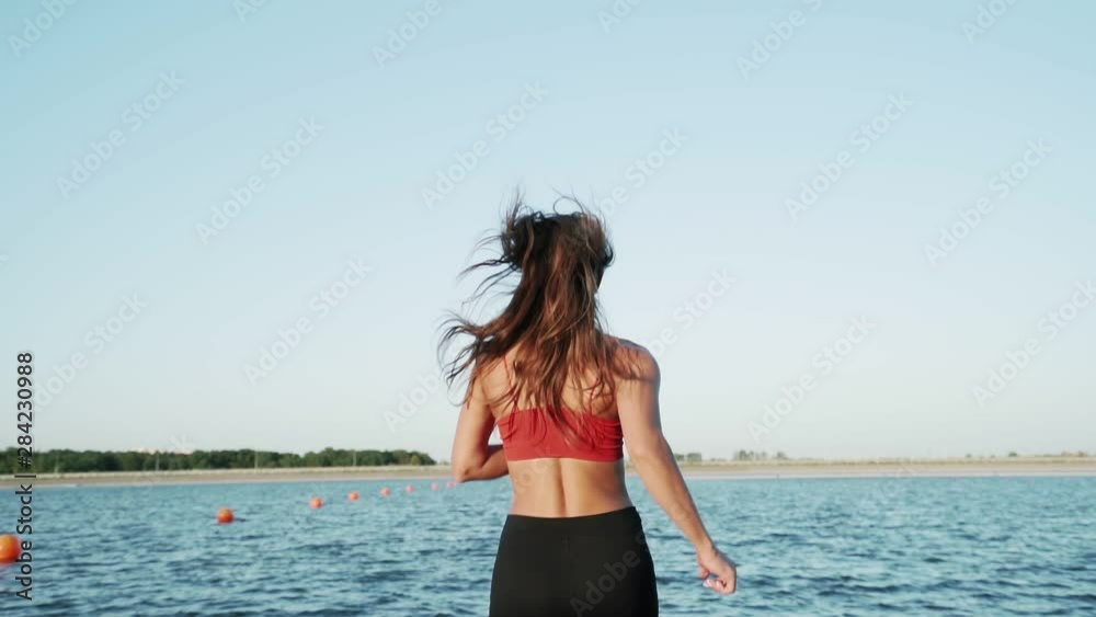 A young athletic Caucasian girl runs along the pantone to the lake. Playing sports. Healthy lifestyle. Slow motion. A young athletic Caucasian girl runs along the pantone to the lake. Playing sports. Healthy lifestyle. Slow motion.