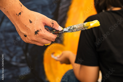 Closeup hand holding yellow oaint brush and yound Asian woman artist painting on the wall. photo