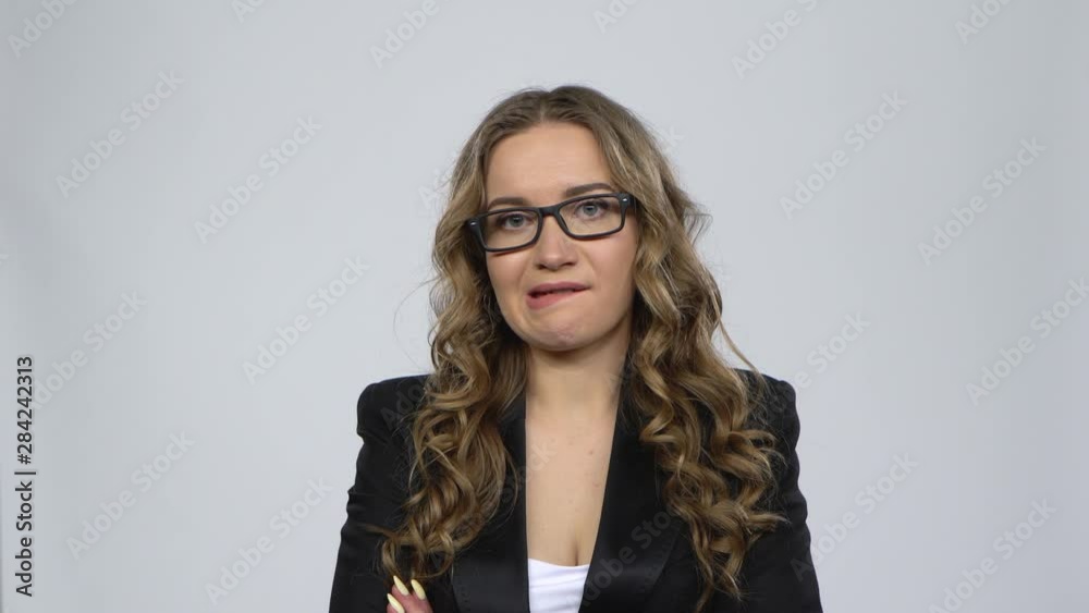 Woman disappointed looks in camera bites her lip then shrugs against grey background Woman disappointed looks in camera bites her lip then shrugs against grey background