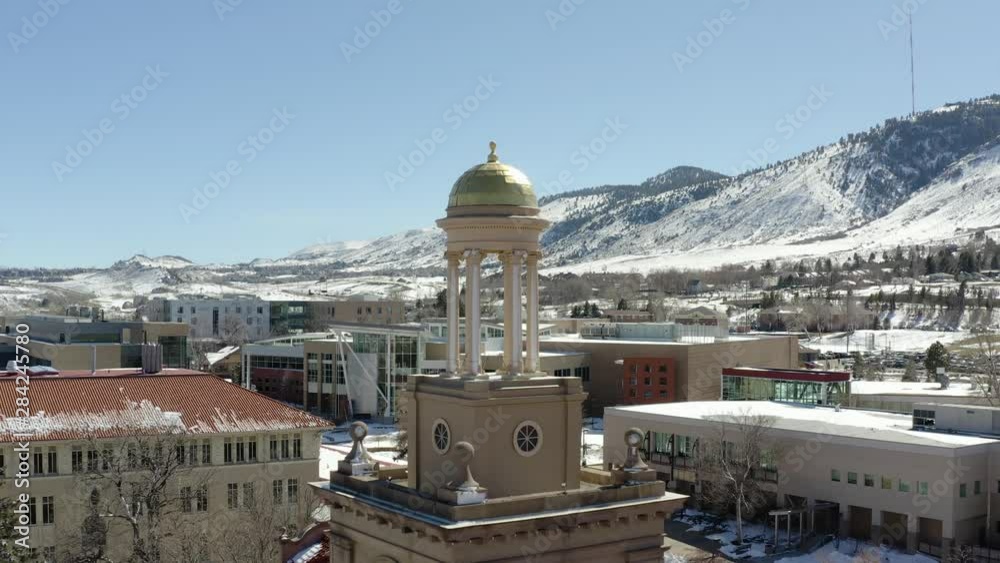 An aerial drone shot moving backwards from a small tower in the middle of a small town overlooking snowy mountains in the winter.