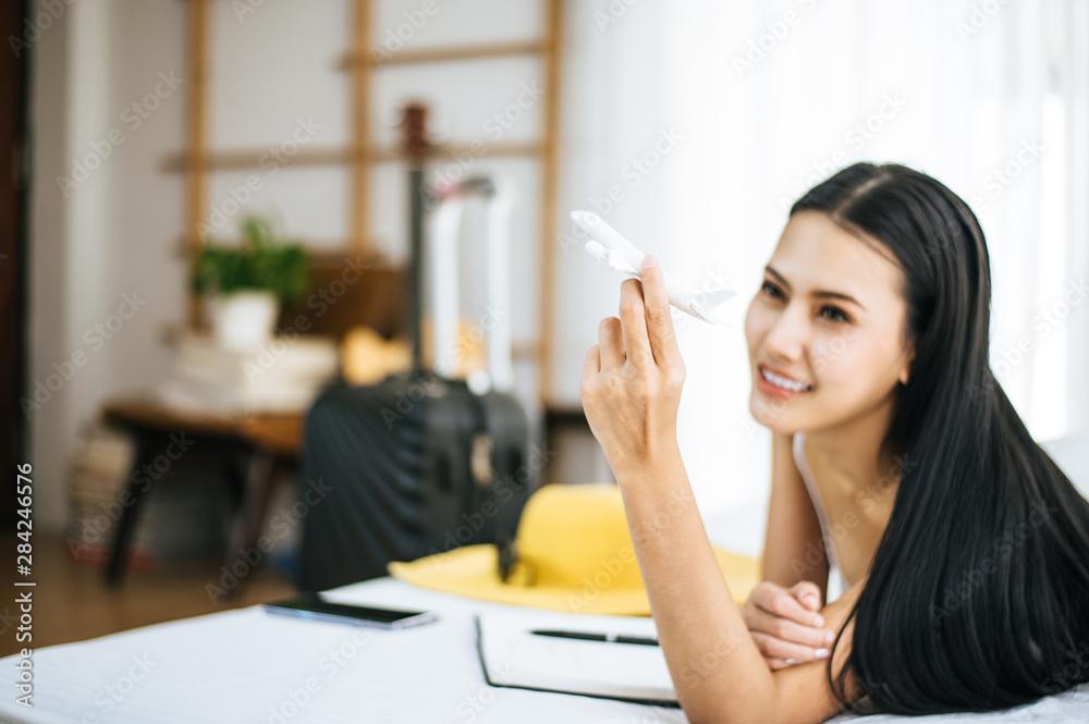 Blured of beautiful asian female hands holding airplane model and planning vacation with travel accessories on bed Blured of beautiful asian female hands holding airplane model and planning vacation with travel accessories on bed