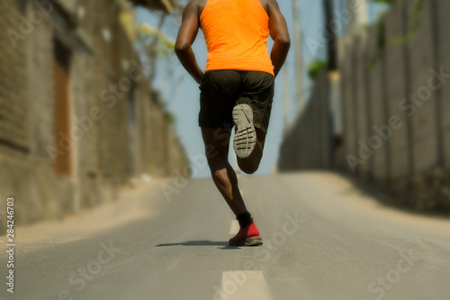 Back view of athletic black African American professional sport man running training hard outdoors on asphalt road during jogging workout in healthy lifestyle