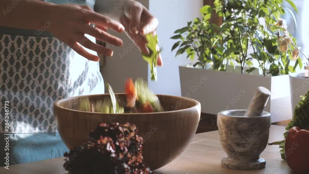 Closeup Of Female Mixing Green Salad by hands In A Bowl on the Kitchen. Side view. Closeup Of Female Mixing Green Salad by hands In A Bowl on the Kitchen. Side view.