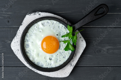 fried eggs in cast iron pan on white wooden stand with parsley