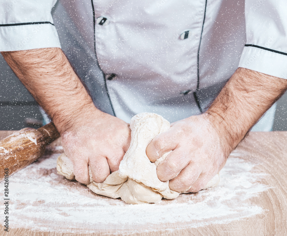 male cook kneads dough on the table