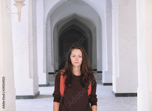 Portrait of a young woman standing in a corridor of white arabian arches in Kalyan Mosque, Bukhara, Uzbekistan