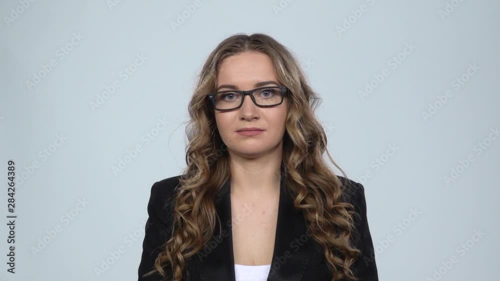 Woman disappointed looks in camera bites her lip then shrugs against grey background, slow motion