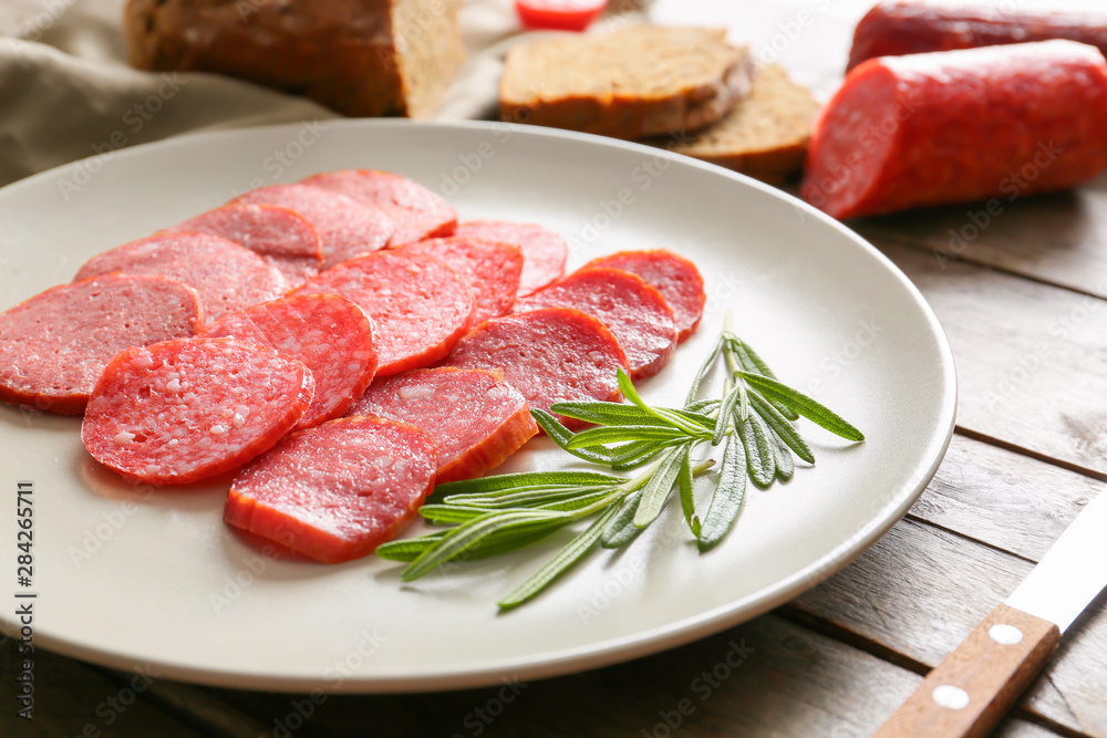Plate with slices of different smoked sausages on wooden table Plate with slices of different smoked sausages on wooden table