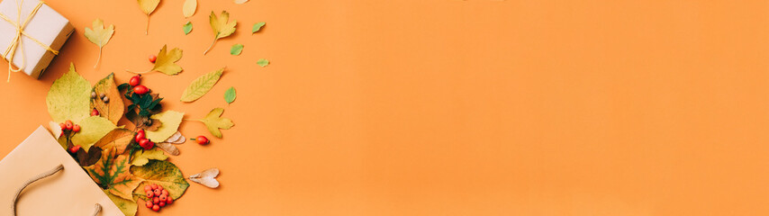 Fall season new collection. Gift box and leaves scattered from shopping bag over orange background. Copy space.