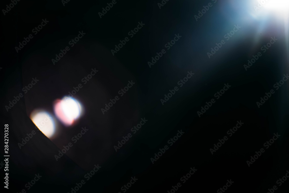 Defocused white lens flare on dark abstract background. Light dots reflection effect.