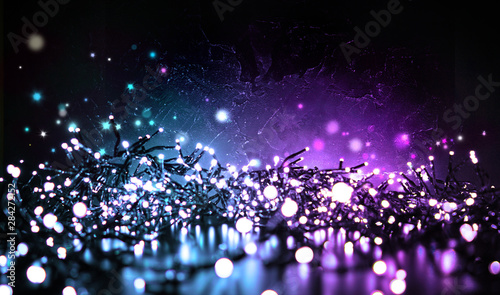 Festive sparkling Christmas lights in evening at night on a dark black textured background. Blue and purple color, copy space.