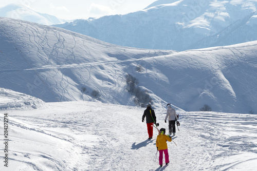 Skiers and snowboarders walk on snowy road at sunny winter morning