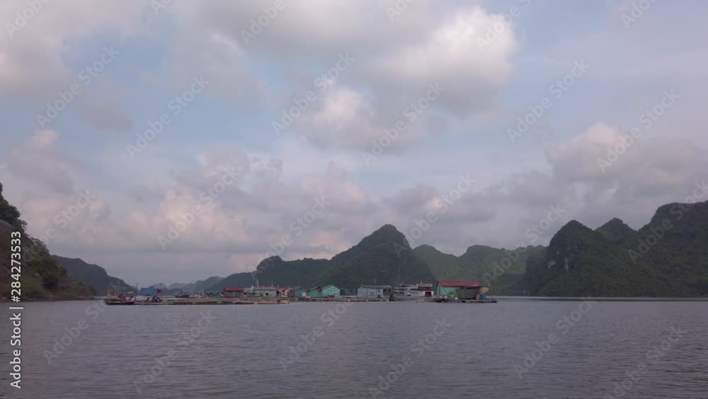 Panoramic view from the sea of fisherman boat village floating on emerald water, Halong Bay at sunset. Background of limestones topped by rainforest jungle. Colorful sky with clouds in the evening. Panoramic view from the sea of fisherman boat village floating on emerald water, Halong Bay at sunset. Background of limestones topped by rainforest jungle. Colorful sky with clouds in the evening.
