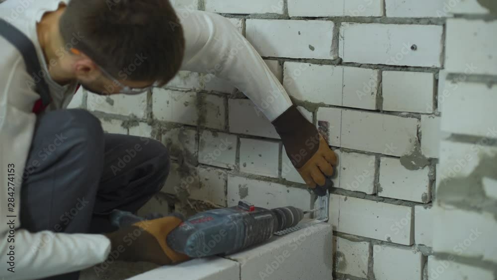 builder making holes in brick wall with electric drill to fix joining clamp builder making holes in brick wall with electric drill to fix joining clamp