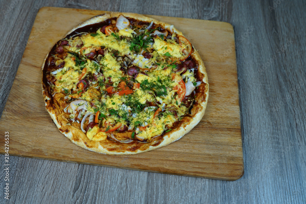 Pizza with mushrooms, sausage cheese and herbs, on a table on a wooden board.     