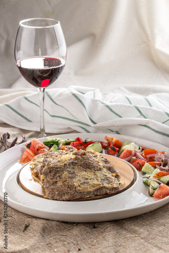 Homemade lamb schnitzel with fresh vegetable salad on the side and glass of red wine on tablecloth Homemade lamb schnitzel with fresh vegetable salad on the side and glass of red wine on tablecloth