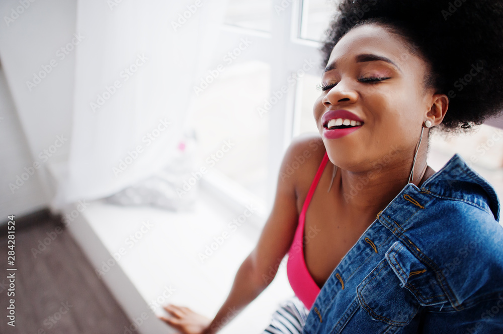 Close up portrait of an attractive african american woman with afro hair wear jeans jacket, posed at white room. Fashionable black model. Close up portrait of an attractive african american woman with afro hair wear jeans jacket, posed at white room. Fashionable black model.
