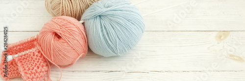 Knitting wool and knitting needles in pastel blue and pink colors on white wooden background banner. top view.copy space