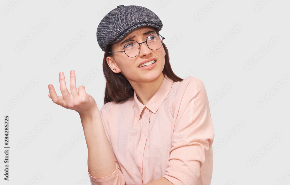 Studio portrait of questioned young woman, looking serious at discussing things, dressed in casual trendy outfit, posing over white wall. Student girl has confused expression. People emotions
