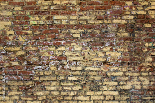 old shabby red brick wall with spots of yellow and white paint. rough surface texture