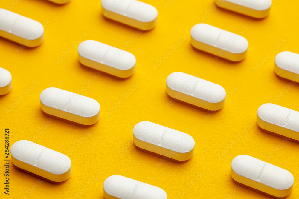 White pills on yellow background. White pills on yellow background.