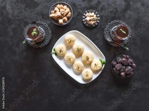 Pedha (Indian sweet), Milk Fudge with tea cups and dates in a black background. Top view photo