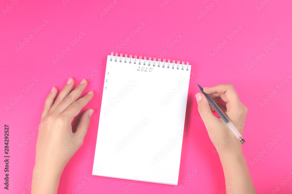 women's hands with manicure write in a notebook for writing on a pink background women's hands with manicure write in a notebook for writing on a pink background