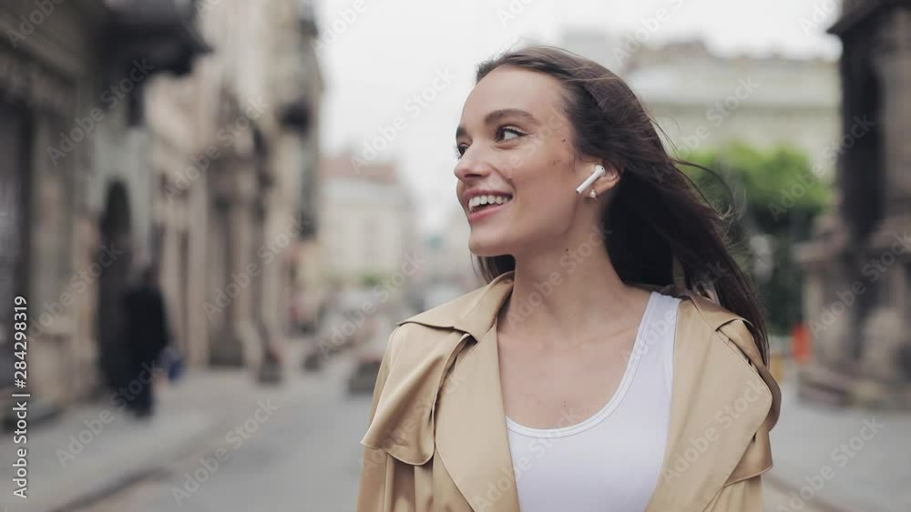 Portrait of Beautiful Happy Young Girl Talking Using Wireless Earphones Smiling Walking Relaxed on the Street City Background Close Up. Portrait of Beautiful Happy Young Girl Talking Using Wireless Earphones Smiling Walking Relaxed on the Street City Background Close Up.
