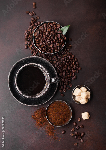 Cup of fresh raw organic coffee with beans and ground powder with cane sugar cubes with coffee tree leaf on brown background.