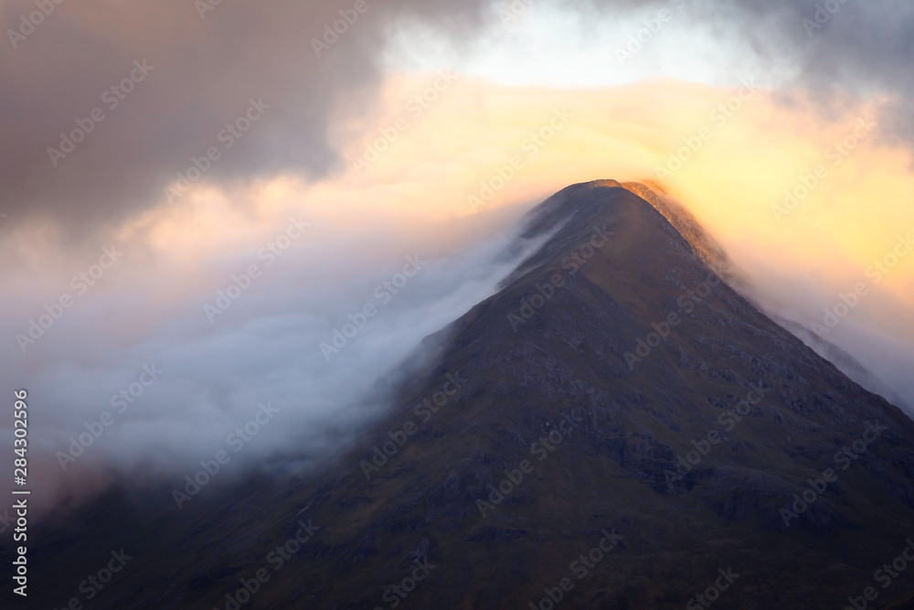 Morning light kissing mountain peak during sunrise in Scottish Highlands.
