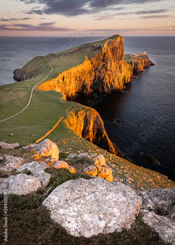 Neist Point, famous landmark with lighthouse on Isle of Skye, Scotland lit by setting sun.