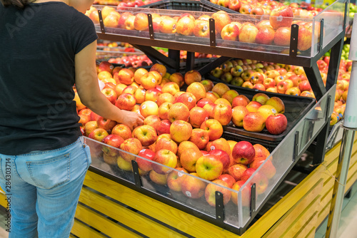 Fresh healthy fruits on shelves in supermarket, with female buyer choosing red apples