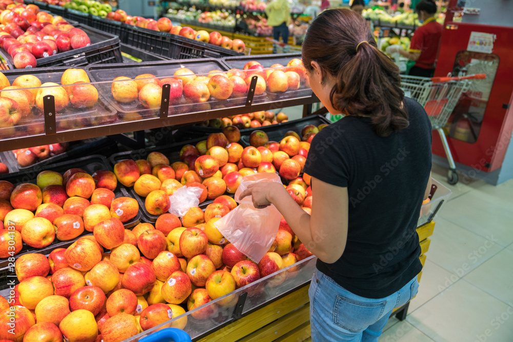 Hands of female buyer choosing red apples in supermarket