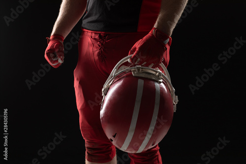 American football player standing with helmet against black background