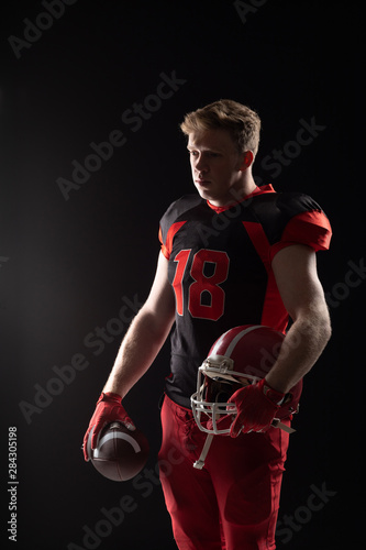 American football player standing with helmet and rugby ball