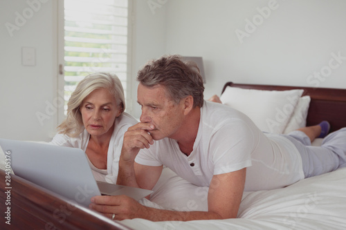 Active senior couple using laptop while lying on bed in bedroom at comfortable home © wavebreak3