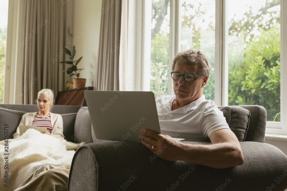 Active senior man sitting on sofa and using laptop in living room at comfortable home Active senior man sitting on sofa and using laptop in living room at comfortable home