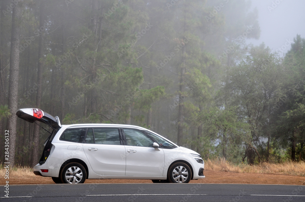 minivan car with open trunk on country road in the forest with fog
