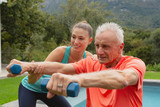 Female trainer assisting active senior man to exercise with dumbbells