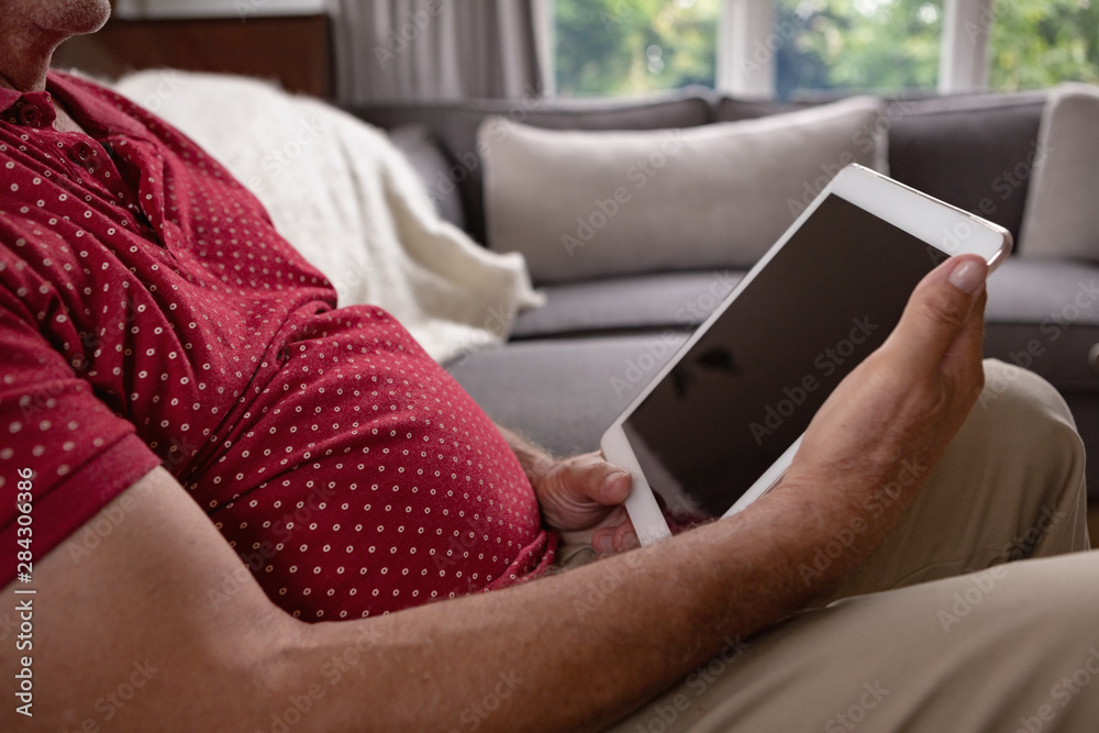 Active senior man using digital tablet on sofa in a comfortable home