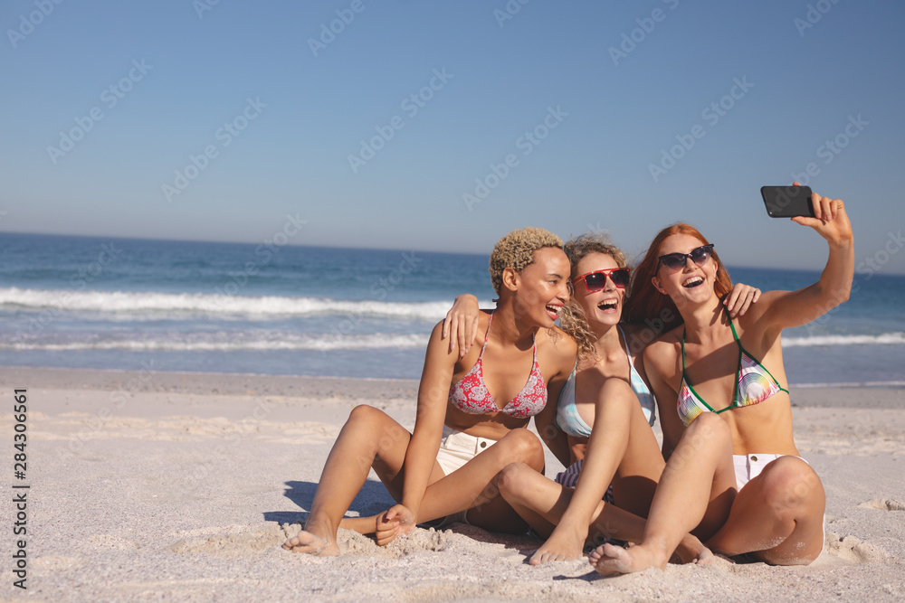 Female friends taking selfie with mobile phone on the beach Female friends taking selfie with mobile phone on the beach