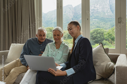 Active senior couple discussing with real estate agent over laptop in living room