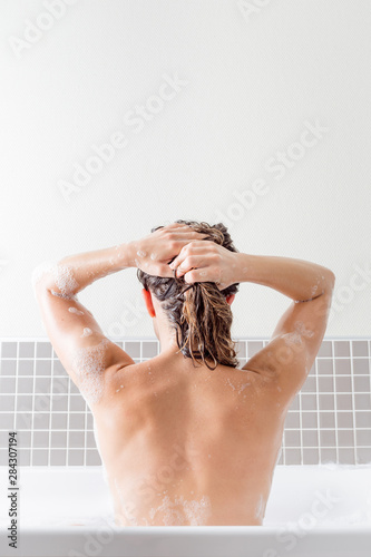Caucasian girl washing her hair inside a bathtub with foam