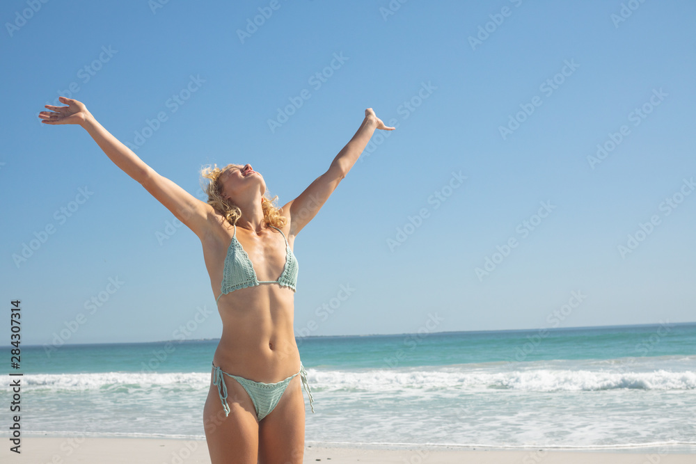 Woman in bikini with arm stretched out standing on the beach Woman in bikini with arm stretched out standing on the beach