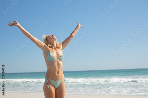 Woman in bikini with arm stretched out standing on the beach  © wavebreak3